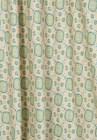 Tessuto crema con un motivo ripetuto di quadrati verdi smerlati e piccole forme floreali blu, mostrato con pieghe morbide.