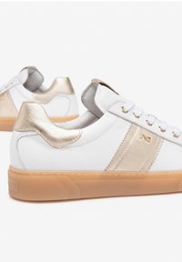White leather sneakers with gold accents, textured panels, and a beige rubber sole. Features classic lace-up design and metallic heel detail.