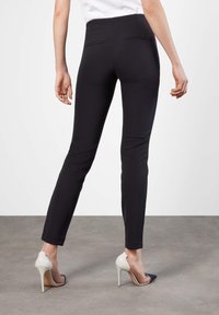 Pantalones ajustados negros con una textura suave, que presentan una cintura alta, bolsillos traseros y una confección elegante, combinados con tacones altos de color claro.