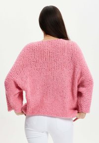 Pink knitted sweater with a loose fit, wide sleeves, and a textured stitch pattern. The back features a rounded neckline and a relaxed silhouette.
