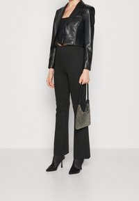 Musta tekonahkainen lyhyt bleiseri, musta toppi, raidalliset levenevät housut ja mustat pistokkaat korkokengät. Hopeinen minilaukku, jossa kimallusta.