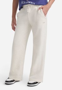 Svetlobežové tepláky vyrobené z mäkkého materiálu, s voľným strihom, elastickým pásom so šnúrkou a bočnými vreckami.