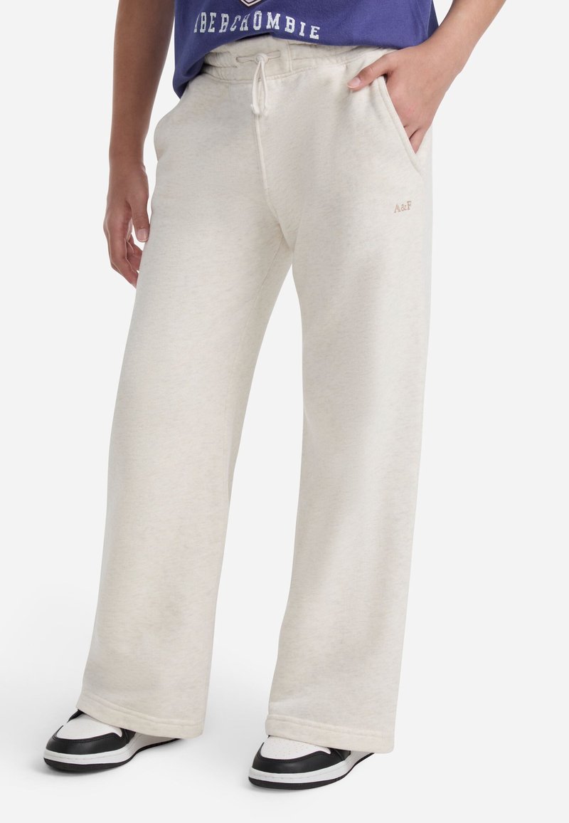 Svetlobežové tepláky vyrobené z mäkkého materiálu, s voľným strihom, elastickým pásom so šnúrkou a bočnými vreckami.