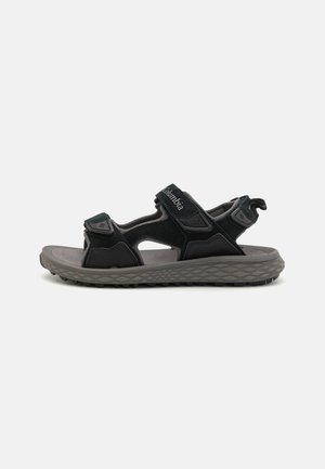 Sandal nero con cinturini regolabili, soletta imbottita e suola in gomma testurizzata con un motivo geometrico. Logo del marchio sul cinturino.