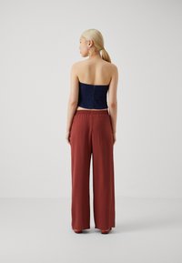 Strapless dark blue denim top paired with loose, ankle-length, rust-colored pants featuring an elastic waistband and smooth texture.