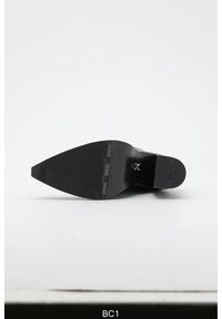 Black high-heeled shoe bottom with a pointed toe, textured rubber sole, and embossed branding on the heel and sole.