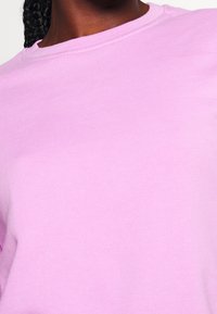 Sudadera de cuello redondo en un suave tono rosa claro, con textura lisa, cuello acanalado y mangas largas casuales, centrada en la simplicidad del diseño.