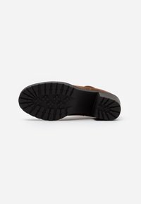 Brauner Lederschuh mit rauer schwarzer Gummisohle und tiefem Profil. Das Obermaterial weist Steppnähte auf. Entwickelt für guten Halt und Langlebigkeit.