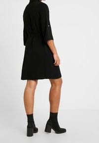 Zwarte jurk met driekwartmouwen, een taille die is aangetrokken en een uitlopende rok. Zachte stof, met een knoopdetail op de mouwen.