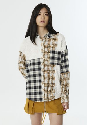 Hemd mit Patchwork-Design: cremefarbener Strukturstoff, schwarz-beige Karomuster, braune Akzente. Lange Ärmel, Knopfverschluss, übergroßer Schnitt.