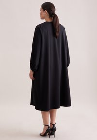 Czarna sukienka midi z długimi, obszernymi rękawami i prostą sylwetką. Wykonana z gładkiej tkaniny, z okrągłym dekoltem i sięgająca poniżej kolan.