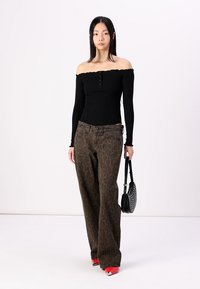 Zwarte off-shoulder top met knopen, bruine broek met luipaardprint in brede pijpen, rode puntige hakken en een zwarte handtas met ronde studs.