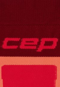 Rote und rosa Kompressionssocke mit dem auffälligen "cep"-Logo in einem kontrastierenden, markanten Design. Hergestellt aus weichem, strukturiertem Stoff mit einem gerippten Muster.