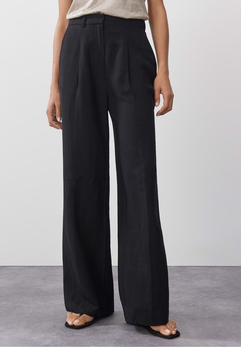 Mustat leveälahkeiset housut, joissa on korkea vyötärö, edessä poimutukset ja sileä, kevyt kangas. Varustettu vyölenkeillä.