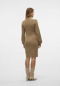 Robe midi à côtes de couleur marron clair, avec des manches longues et une silhouette ajustée. Complétée par des bottines beige à la cheville.