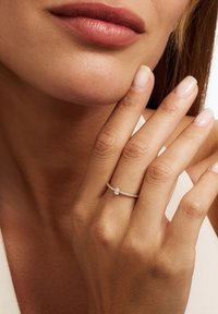 Een gouden ring met een peervormige diamant als centraal element, omringd door een band die versierd is met kleine heldere stenen, met een delicate, gestructureerde afwerking.