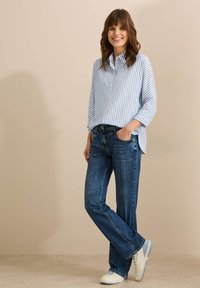 Camisa de manga larga a rayas azul y blanca con cuello, combinada con jeans de mezclilla azul y zapatillas blancas; corte relajado, tejido texturizado.