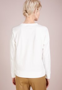 Sudadera blanca de algodón con un corte relajado, que presenta un cuello redondo y mangas largas. El dobladillo y los puños son de canalé para aportar textura.