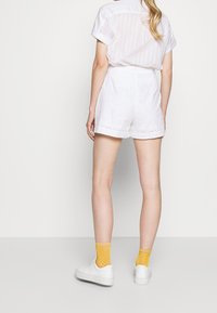 Hvid kortærmet skjorte, hvide broderede shorts med bladmønstre, parret med hvide sneakers og gule strømper med hvide prikker.