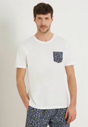 Tricou alb din bumbac, cu guler rotund și mâneci scurte. Prezintă o buzunare modelat în navy, cu motive marine în verde și alb.