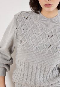Hellgrauer gestrickter Pullover mit einem strukturierten Rautenmuster oben, geripptem Halsausschnitt und Bündchen sowie einem Kabelstrickunterteil.