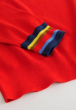 Red knitted sweater cuff featuring contrasting stripes in blue, yellow, and red. Smooth texture with a ribbed finish at the edges.