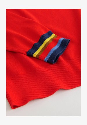 Red knitted sweater cuff featuring contrasting stripes in blue, yellow, and red. Smooth texture with a ribbed finish at the edges.