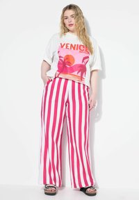 Bílý grafický tričko s designem "Venice Beach" v růžové a oranžové barvě. Pruhované kalhoty v jasně růžové a bílé, široké nohavice, s volným střihem.