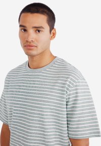 Pruhované tričko v světle modré a bílé barvě, krátké rukávy, kulatý výstřih, jemná textura, volný střih, s vodorovnými pruhy.
