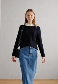 Mornarska jopica z dolgimi rokavi nad belim srajčnim ovratnikom, v kombinaciji s svetlo modrim jeans krilom in majhno črno torbico.