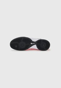Semelle d’une chaussure de sport avec une bande de roulement en caoutchouc noir et un logo Nike Swoosh blanc sur la zone de la voûte plantaire, sur un fond gris clair.