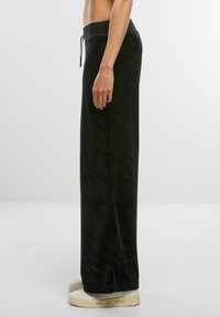 Schwarze Samohosen mit entspannter Passform, ausgestattet mit einem elastischen Bund und Kordelzug. Gemusterte Textur und leicht ausgestellte Beine.