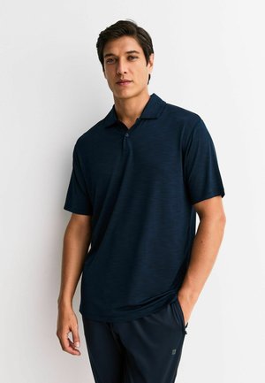 Tumši zils īsroku polo krekls ar teksturētu audumu, tam ir apkakle un pogu josla. Valdīts kopā ar tumšām biksēm, kas atbilst krāsai.