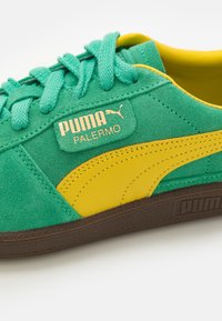 Baskets Puma Palermo en daim vert avec une bande en cuir jaune, lacets assortis et semelle marron sur fond blanc.