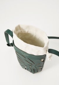Grüne Lederhandtasche mit durchbrochenem Blätterdesign, beigem Stofffutter, Kordelzugverschluss und verstellbarem Tragegurt. Mit Logodetail.