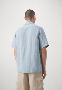 Camicia azzurra chiara a maniche corte realizzata in tessuto testurizzato, con colletto e vestibilità comoda, mostrata da dietro.