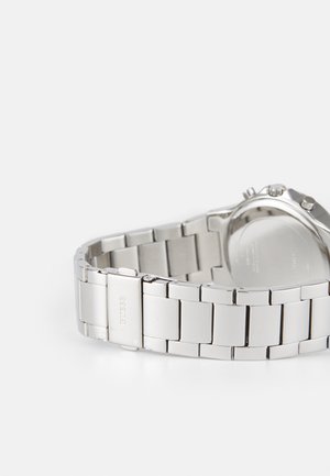 Sidabrinė nerūdijančio plieno laikrodis su susietu apyrankės dizainu, apvaliu korpusu ir minimalistiniu ciferblatu. Yra poliruotos ir šlifuotos metalinės tekstūros.