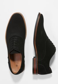 Chaussures à lacets en suède noir avec une tige texturée, semelle contrastante marron et design hauteur cheville. Dotées d'une doublure en cuir lisse et de coutures détaillées.