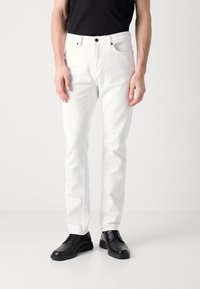 Witte denim spijkerbroek met een slim fit, vijf-pocket ontwerp, contrasterende zwarte stiksel en een standaard tailleband, gedragen met zwarte veterschoenen.