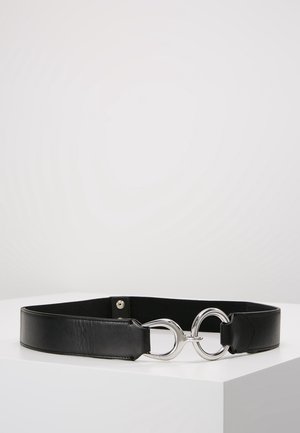 Czarny pasek ze skóry ze szerokim paskiem i charakterystyczną srebrną sprzączką w kształcie przeplatających się pętli na białej powierzchni.