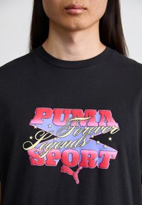 Juodas medvilninis marškinėliai su spalvinga grafika, kurioje yra tekstas "PUMA Amžinai Legendos SPORT" ir Puma logotipas kontrastingame dizaine.