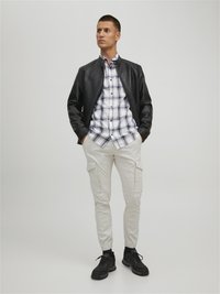 Black leather jacket over a white and navy plaid shirt, paired with light cargo pants and black sneakers; features include buttons and pockets.