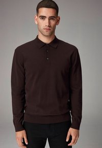 Polo de manga larga marrón oscuro con cuello y tapeta de tres botones. Los puños y el dobladillo acanalados ofrecen un aspecto ajustado.