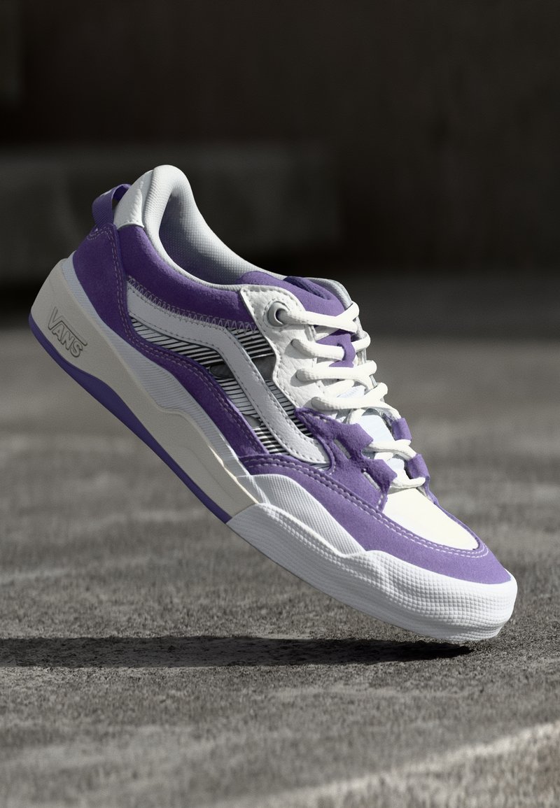 Zapatilla morada y blanca con superficie texturizada, diseño en capas, acentos a rayas y acolchado en el cuello. Suela ligera con detalle de logo.