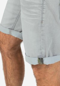 Light blue denim shorts with rolled hems, featuring subtle wear patterns and a camouflage accent at the hem.
