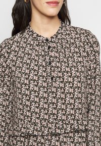 Černé květinové šaty se vzorem malých růžových a bílých květin, výraznou texturou, kulatým výstřihem a knoflíkovým detailem na přední straně.