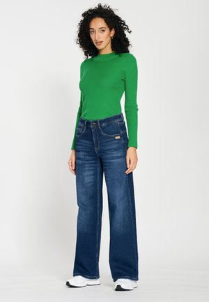 Green ribbed long-sleeve top paired with high-waisted dark blue wide-leg jeans. The outfit is complemented by white sneakers.