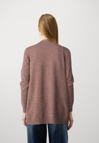 Sweter kardigan w kolorze brudnego różu, z luźnym krojem, prążkowanymi mankietami i dołem, oraz długimi rękawami. Noszony na ciemnych dżinsach, o gładkiej fakturze.