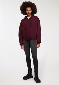 Felpa borgogna con zip e lacci, tasche frontali, abbinata a jeans skinny scuri e stivaletti neri con lacci. Texture del tessuto liscia.