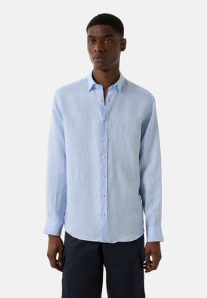 Lichtblauwe blouse met lange mouwen van linnen, voorzien van een button-down kraag, witte knopen en een geborduurd logo op de borst. Zachte textuur en een ontspannen pasvorm.